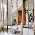 Interior view of a home under renovation with exposed wooden beams and door.